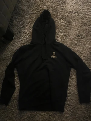 Svart hoodie från Morris med tryck - Svart hoodie från Morris med guldfärgat tryck och logga på bröstet. Klassisk huva med snörning och långa ärmar. Perfekt för en chill och stilren look. Passar perfekt om du är runt 180. Står M i den
