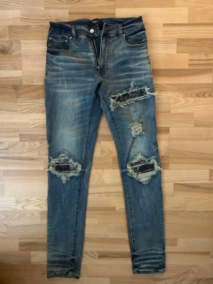 Amiri Blå slitna jeans med bandana patchdetaljer - Säljer ett par blå Amiri jeans med skinny fit och tydliga slitningar samt patchade hål på benen. Jeansen har klassisk femficksdesign och dragkedjegylf. De har en cool, streetinspirerad look med kontrasterande tyg under de trasiga partierna.