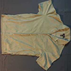 Ljusgrön kortärmad skjorta H&M - Säljer en ljusgrön kortärmad skjorta från H&M i regular fit. Skjortan har klassisk krage, knäppning framtill och en bröstficka. Materialet är mjukt och frottéliknande, perfekt för en avslappnad stil.