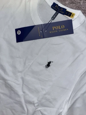 Vit t-shirt från Polo Ralph Lauren - Klassisk vit t-shirt från Polo Ralph Lauren med den ikoniska broderade loggan på bröstet. T-shirten har rund halsringning och korta ärmar. Tillverkad i mjuk bomull för en skön och stilren look.