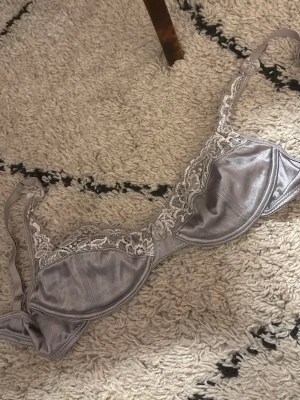 Ljuslila spets-bh med rosetter storlek 75 B - Säljer en ljuslila bh med vacker spetsdetalj upptill och små rosetter framtill och på axelbanden. Bh:n har bygel och tunna, justerbara axelband. Materialet är glansigt och ger en lyxig känsla. Perfekt för dig som gillar feminina detaljer. Ops inga metall grejer i bhn 