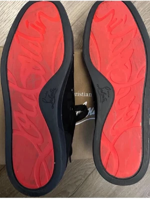 Christian Louboutin svarta sneakers - Svarta sneakers från Christian Louboutin i mocka med klassisk röd sula och snörning. Snygg och stilren design med diskreta detaljer och signaturlogga under sulan. Perfekta för dig som vill ha något exklusivt och trendigt.