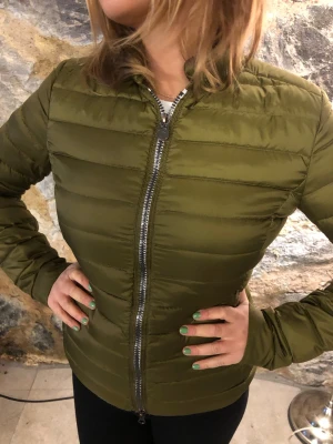 Olivgrön dunjacka från Colmar - Snygg olivgrön dunjacka från Colmar med quiltad design och rak passform. Jackan har en silverfärgad dragkedja framtill och Colmar-logga på ärmen. Perfekt för kalla dagar och enkel att matcha med olika outfits.