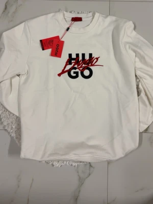 Vit sweatshirt från Hugo med tryck - Vit sweatshirt från Hugo med svart och rött logotryck på bröstet. För stor för mig och kan ej lämna tillbaka, köpt för 1300