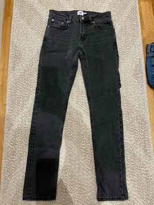 Svarta slim jeans från 157 - Snygga svarta slim fit jeans från 157 med klassisk femficksdesign och knappgylf. Jeansen har en smal passform och är tillverkade i ett mjukt denimtyg som ger en bekväm känsla. Perfekta för dig som gillar en stilren och enkel look.
