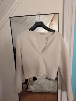 Beige cropped kofta från Gina Tricot - Mysig beige kofta från Gina Tricot med lång ärm och croppad passform. Koftan har rund halsringning och knäppning framtill med små knappar. Tillverkad i ett mjukt, fluffigt material som känns skönt mot huden.