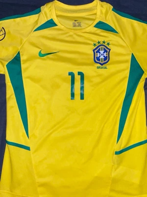 VM Brasilien Nike fotbollströja - Brasilien fotbollströja från VM 2002, med Ronaldihno på ryggen. Passar både M och L. En legendarisk tröja som passar till vardagen, men även till sportiga sammanhang.