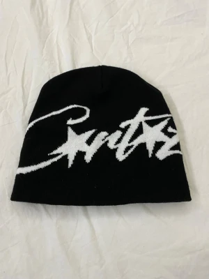 Svart Corteiz mössa - Svart mössa från Corteiz. Klassisk passform och mjukt stickat material som håller dig varm. Perfekt accessoar för en streetwear-look.