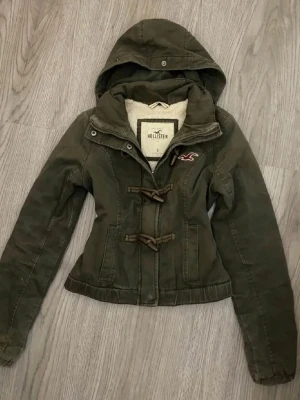 Grön jacka med huva från Hollister - Snygg grön jacka från Hollister med huva och mysigt foder. Säljer den då den inte passade mig som är 175cm lång men är super snygg❤️Pris går att diskutera❤️