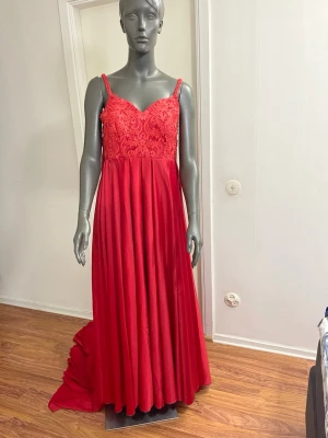 Röd långklänning med spetsdetaljer - Elegant röd långklänning med smala axelband och v-ringad överdel dekorerad med vacker spets. Kjolen är vid och faller snyggt ner mot golvet. Perfekt för speciella tillfällen när du vill sticka ut.lätt att storleksjustering storlek 