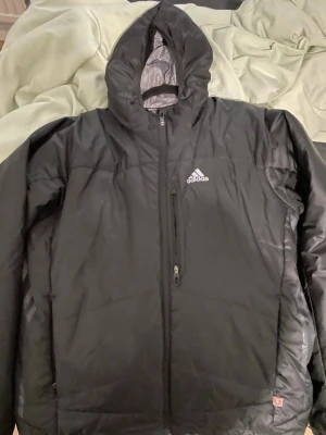 Adidasjacka - Svart jacka med dragkedja och luva från Adidas Outdoor. Jackan har en liten Adidas logga på bröstet. Det är UK 44/46