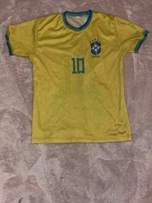 Brasilien Neymar Jr 10 matchtröja - Gul Brasilien fotbollströja med gröna detaljer, Neymar Jr och nummer 10 på ryggen. CBF-logga på bröstet. Perfekt för dig som älskar fotboll och vill stötta Brasilien. Kortärmad och rund halsringning.