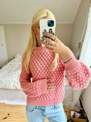 Rosa bubblig stickad tröja - Superfin rosa stickad tröja med bubbligt mönster och ballongärmar. Tröjan har ribbade muddar vid hals, ärmslut och nederkant. Perfekt för dig som vill ha en mysig och trendig look. Materialet känns mjukt och skönt mot huden.