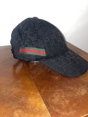 Svart Gucci keps modell canvas - Snygg svart keps från Gucci i modellen canvas med klassiskt GG-monogram över hela kepsen. Kepsen är i tygmaterial och har böjd skärm. Perfekt för dig som vill ha en stilren accessoar med lyxig känsla.