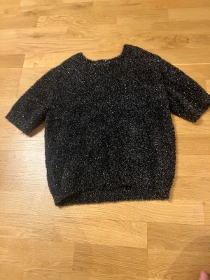 Svart glittrig stickad tröja - Cool svart stickad tröja med glittrigt garn och kortare ärmar. Tröjan har en rak passform och är perfekt för att ge outfiten lite extra shine. Materialet känns mjukt och lite fluffigt.