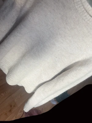 Beige stickad tröja med rund hals - Mysig beige stickad tröja med rund halsringning och ribbade muddar vid ärmslut och nederkant. Tröjan har en avslappnad passform och är perfekt för lager-på-lager-stil under kyliga dagar.