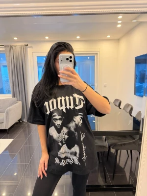 Svart Tupac t-shirt med tryck - Cool svart t-shirt med stort Tupac-tryck framtill i vitt och grått. Oversized passform och korta ärmar. Perfekt för dig som gillar streetwear och hiphop-inspirerad stil.