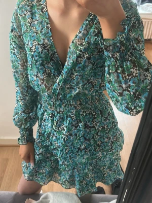 Blommig omlottklänning i grönt och blått - Klänning från Zara köpte typ 2023 men den e fortfarande i bra skick för var knappast använt men den är väldigt fin!