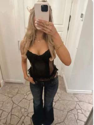 Svart spetsbustier med volangkant - Korsetten har slutat tillverkas, och är svåra att hitta därav priset. Trendig svart bustier i mesh och spets med volangkant nedtill och vadderade kupor. Märket är H&M