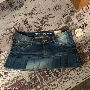 Mörkblå plisserad jeanskjol Replay - Supersnygg mörkblå jeanskjol från Replay med plisserad nederkant och slitna detaljer. Kjolen har klassiska fem fickor, knappgylf och cool tvättad look. Perfekt för dig som vill ha en trendig och edgy stil. Storlek 170 men passar som xs/s. Sytt volangen dit själv