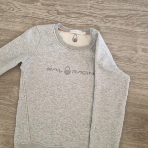 Grå Sail Racing sweatshirt XS - Mysig grå sweatshirt från Sail Racing i storlek XS. Tröjan har rund halsringning, lång ärm och Sail Racing-logga framtill. Insidan är fodrad med mjuk fleece för extra komfort. Perfekt för kyliga dagar.