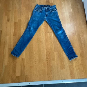 Blå Replay anbass jeans - Säljer ett par blå replay anbass jeans med klassiska fem fickor och snygga kontrastsömmar på bakfickorna. Jeansen har normal midja och är tillverkade i stretchig denim för en snygg passform. Hör av dig vid minsta fråga eller mer bilder!