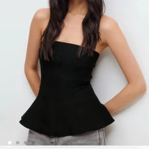 Svart axelbandslös korsettopp - Snygg svart korsettopp med axelbandslös design och figurnära passform. Toppen har en lätt utsvängd nederkant som ger en cool siluett. Perfekt att styla med jeans eller kjol för en trendig look. Pris går att diskutera 💕