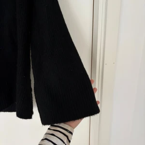 Svart stickad polotröja - Mysig svart stickad polotröja med lång ärm och relaxed fit. Tröjan har en hög krage och är ribbstickad i både ärmslut och nederkant. Perfekt för kalla dagar när du vill vara både bekväm och stilren.