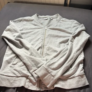 Ljusgrå bomberjacka - Snygg ljusgrå bomberjacka från Lager 157 med dragkedja framtill och ribbade muddar vid ärmslut och midja. Jackan är i mjuk bomull och har två fickor på sidorna. Perfekt för en chill och stilren look.