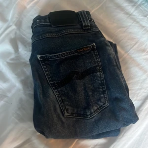 Mörkblå jeans från Nudie Jeans 28/30 - Snygga mörkblå jeans från Nudie Jeans med klassisk femficksdesign och broderad bakficka. Jeansen har en rak passform och är tillverkade i slitstarkt denimtyg. Perfekta för dig som gillar stilrena och tidlösa jeans. Skinny