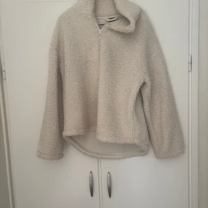 Beige fleece-tröja från Gina Tricot - Mysig beige fleece-tröja från Gina Tricot i storlek S. Tröjan har halv dragkedja framtill, hög krage och långärmad modell. Perfekt för kyliga dagar och supermjuk med teddystruktur. Passformen är lite loose och den är något längre bak.