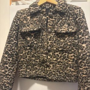 Leopardmönstrad jacka med fickor - Snygg leopardmönstrad jacka med stora bröstfickor och markerad krage. Jackan är croppad och har knappar framtill. Utsidan är i mjukt material och insidan är fodrad med svart tyg. Perfekt statement-plagg för dig som vill sticka ut.