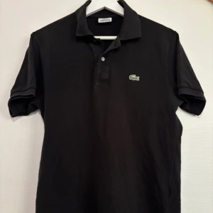 Lacoste piké  - Snygg svart piké från Lacoste i storlek 3, motsvarar medium. Pikén är i gott skick och har inga defekter.   Vid fler bilder eller frågor är det bara att höra av sig, och kom ihåg, alltid 14 dagars ångerrätt hos oss på Revalo🤝👕