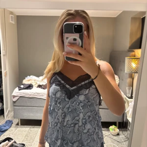 Linne från Zadig - Zadig linne. Säljer en snygg grå linnetopp med svart spetsdetalj längs v-ringningen. Toppen har ett ormmönstrat print och tunna axelband. Perfekt att styla med jeans eller kjol för en trendig look.