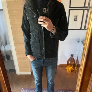 Svart jeansjacka  - Säljer en riktigt fet svart jeansjacka med  knappdetaljer. Jackan har en rak passform och klassisk krage, perfekt för dig som gillar en avslappnad men stilren look. Materialet är denim och jackan har tryckknappar framtill. Size medium. Tags och liknande har klippts bort från jackan. Bara skriva vid frågor!😃