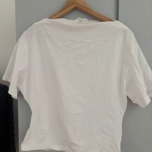 Vit basic t-shirt i bomull - Enkel vit t-shirt i klassisk modell med rund hals och korta ärmar. Tillverkad i mjuk bomull, perfekt för en clean och avslappnad stil. Passformen är normal och t-shirten är helt utan tryck eller mönster.