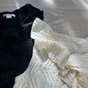 2 st volangtoppar från Gina Tricot, svart & vit - Två snygga ärmlösa toppar från Gina Tricot i storlek 158/164. En i svart och en i vit, båda med volangdetaljer framtill och ett strukturerat, lätt transparent tyg. Perfekta för att lyfta vilken outfit som helst med sin coola volanglook.