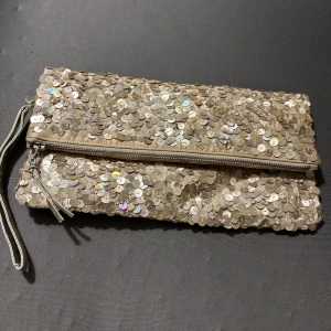 Glittrig kuvertväska med paljetter - Snygg kuvertväska täckt av glittrande paljetter i silverton. Väskan har dragkedja och en liten handledsrem. Perfekt accessoar för att lyfta din outfit med extra bling.