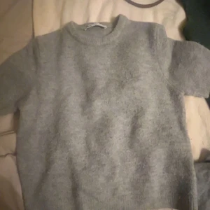 Grå stickad kortärmad tröja - Mysig grå stickad tröja med korta ärmar och rund halsringning. Perfekt för lager-på-lager och passar till både jeans och kjol. Enkel och stilren design som funkar året runt.