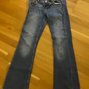 Blå jeans från Gina Tricot, stl 158 - Snygga blå jeans från Gina Tricot i storlek 158. Jeansen har klassisk femficksdesign, raka ben och coola slitningar framtill. Bakfickorna har lock med knappdetalj. Perfekta för dig som gillar en avslappnad och tidlös look.
