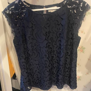 Mörkblå spetsblus Holly & Whyte - Säljer en mörkblå blus från Holly & Whyte by Lindex i storlek M. Blusen är ärmlös med vackert spetsmönster och rund halsringning. Perfekt för dig som gillar detaljer och stilren look.