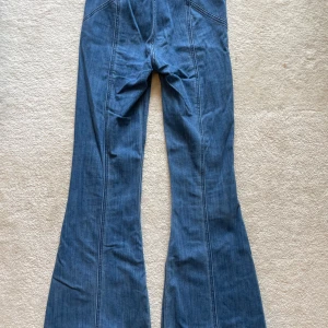 Express blå bell flare jeans med avtagbart bälte - Otroligt snygga blå bell flare jeans från Express med hög midja och bälte. Jeansen har markerade sömmar, dragkedja och är tillverkade i stretchigt denim. Perfekta för dig som gillar en retroinspirerad look med extra vidd nertill och kramar bakdel, höfter och lår väldigt smickrande. 
