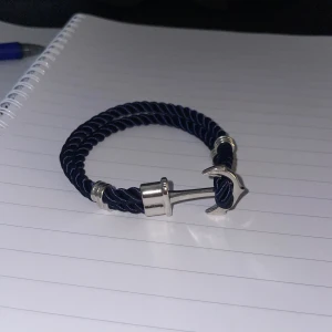 Ankare armband i blått & silver - Snyggt armband med marinblått tvinnat rep och detaljer i silverfärgad metall. Stängs med ett coolt ankare som ger en nautisk vibe. Perfekt accessoar för dig som gillar stilrena och unika smycken.