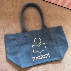 Blå shoppingväska Isabel Marant  - Snygg blå shoppingväska från Isabel Marant i jeansmaterial med stort vitt logotryck framtill. Väskan har dubbla handtag och rymligt fack med dragkedja inuti. 