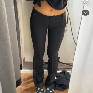 Svarta kostymbyxor med låg midja - Säljer ett par svarta kostymbyxor med låg midja och raka ben. Byxorna har bälteshällor, fickor bak och klassisk stängning fram. Snygg passform som sitter tajt över höfterna och låren, perfekt till en trendig look.