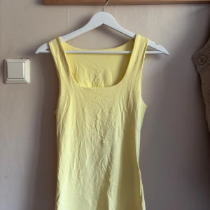 Gul linnetopp från ONLY - Snygg ljusgul linnetopp från ONLY med breda axelband och rundad halsringning. Superenkel att matcha med jeans eller kjol för en fräsch look.