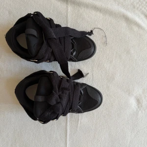 Lanvin curb skor Size43 - Unika svarta sneakers med chunky siluett och extra breda svarta snören. Skorna har rund tå, platt sula och detaljer i både mocka och syntet. Metallöglor ger en cool touch och den helsvarta looken passar perfekt till streetwear.