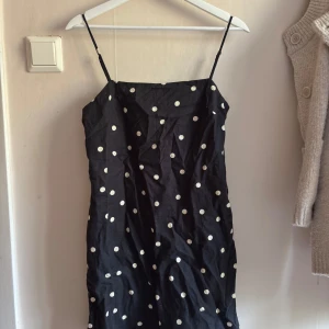 Svart prickig klänning H&M linne - Svart kort klänning från H&M i linneblandning med vita prickar. Smala axelband och rak passform ger en enkel och stilren look. Perfekt för dig som gillar klassiska mönster och lätt material.