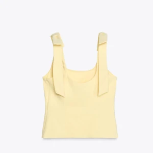 Gul linnetopp med knytband - Söt ljusgul linnetopp med breda axelband som knyts i rosetter. Toppen har en rak passform och är tillverkad i ett mjukt bomullsliknande material. Perfekt för varma dagar och ger en fräsch look med sina fina detaljer på axlarna.