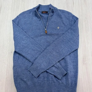 Blå stickad tröja från Morris XL - Snygg blå stickad tröja från Morris i storlek XL men sitter som L skulle jag säga jag är 185 och den passar mig Tröjan har ribbad krage, half zip-dragkedja och en broderad logga på bröstet. Perfekt för lager-på-lager och chill stil under höst och vinter.